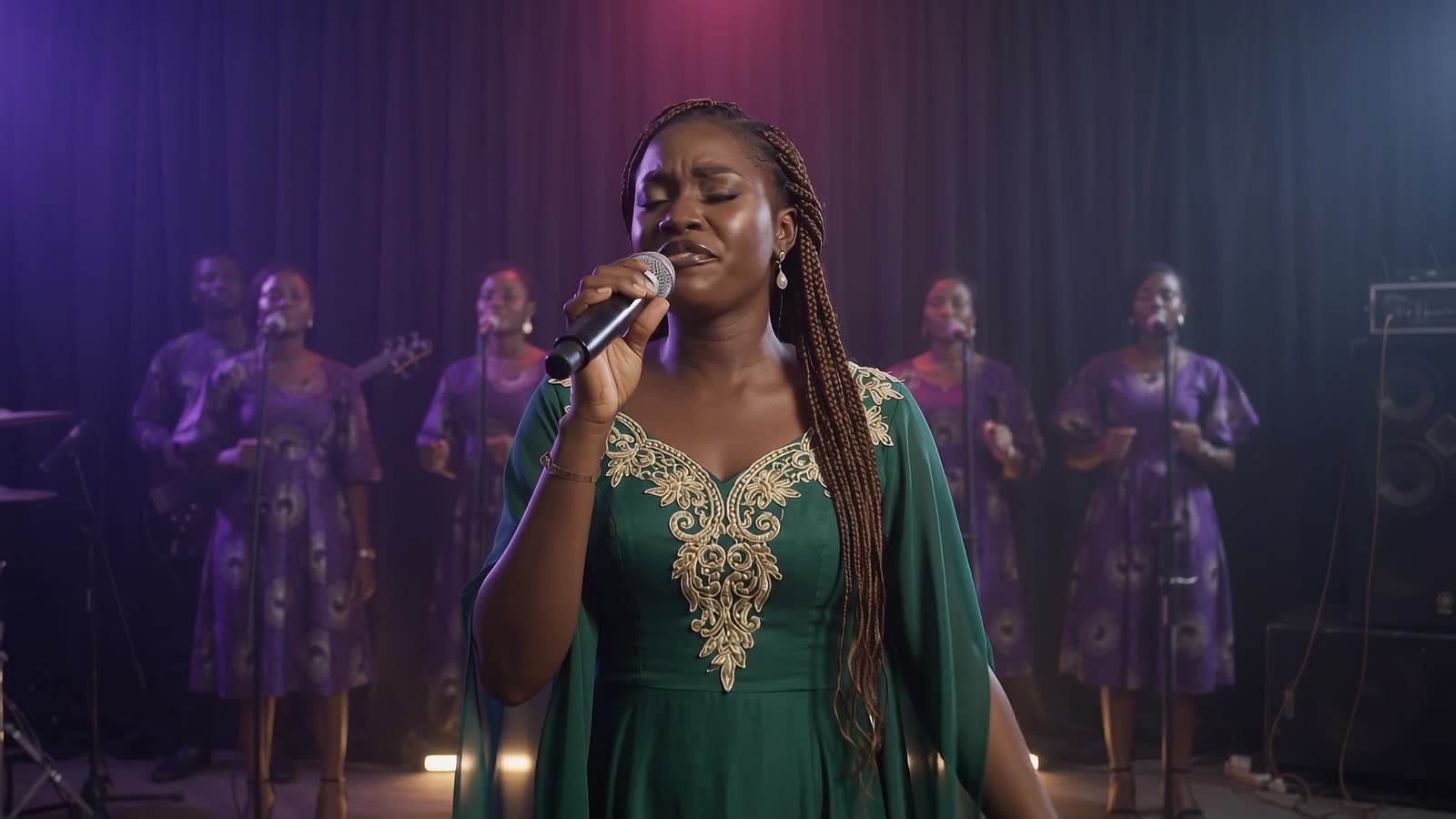 A singer in green at the microphone, her choir in matching dresses behind her under stage light.